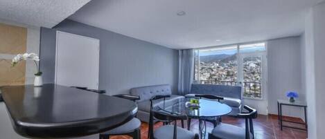 A modern living room with a dining area, large windows, and a view of a cityscape.
