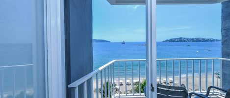 A balcony with a view of the sea, a chair, and a table.