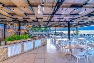 Un área de comedor al aire libre con vistas al mar, techada con madera y amueblada con sillas y mesas blancas.
