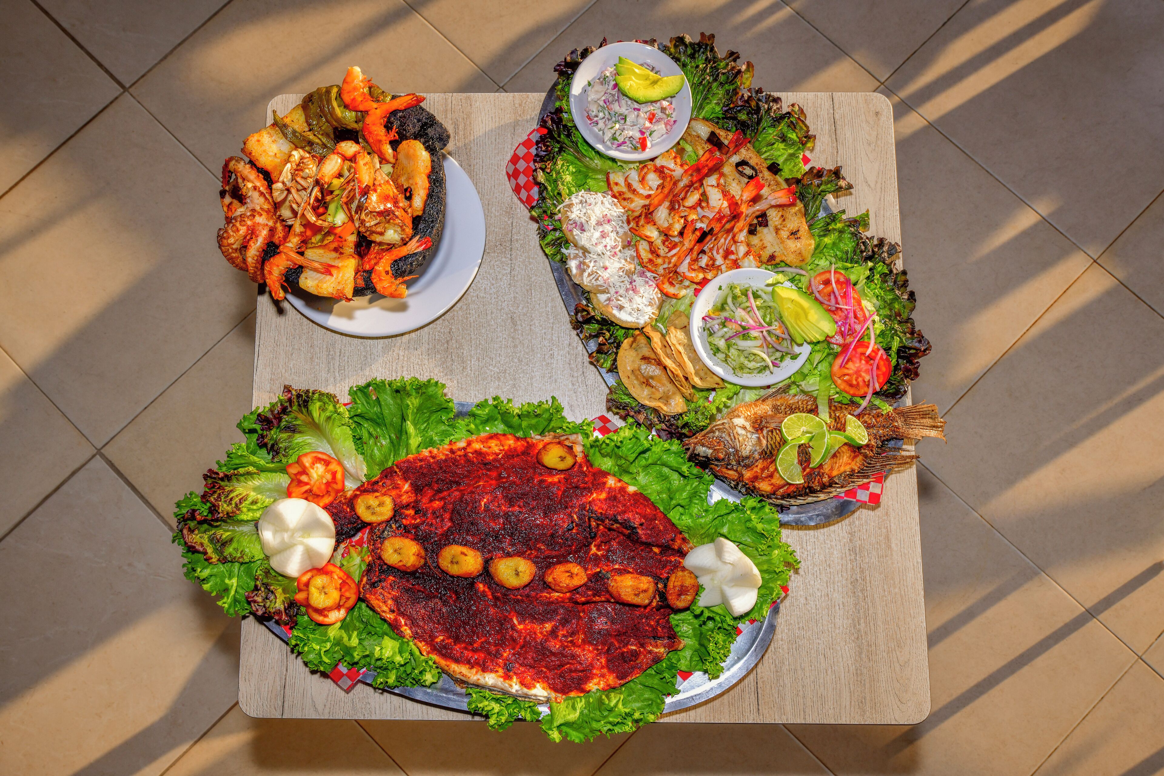 Una mesa con varios platos, incluyendo mariscos a la parrilla, ensaladas y un pescado grande.