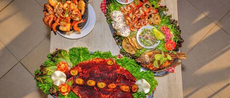 Una mesa con varios platos, incluyendo mariscos a la parrilla, ensaladas y un pescado grande.