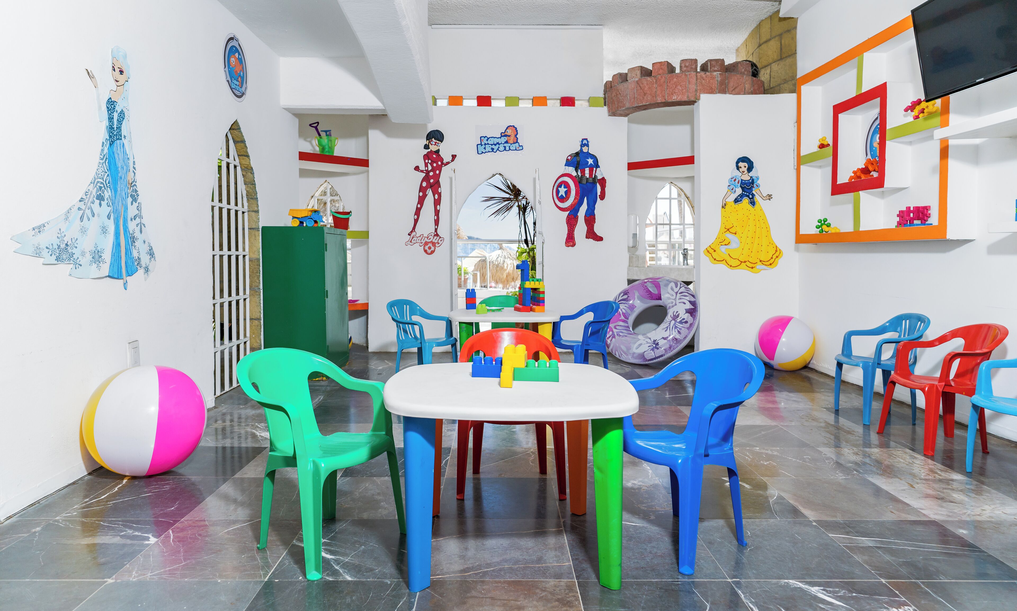 A children's playroom with colorful chairs, a table, and various toys.