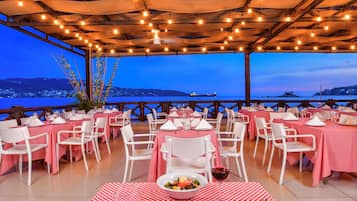 An outdoor dining area with checkered tablecloths, white chairs, and string lights.