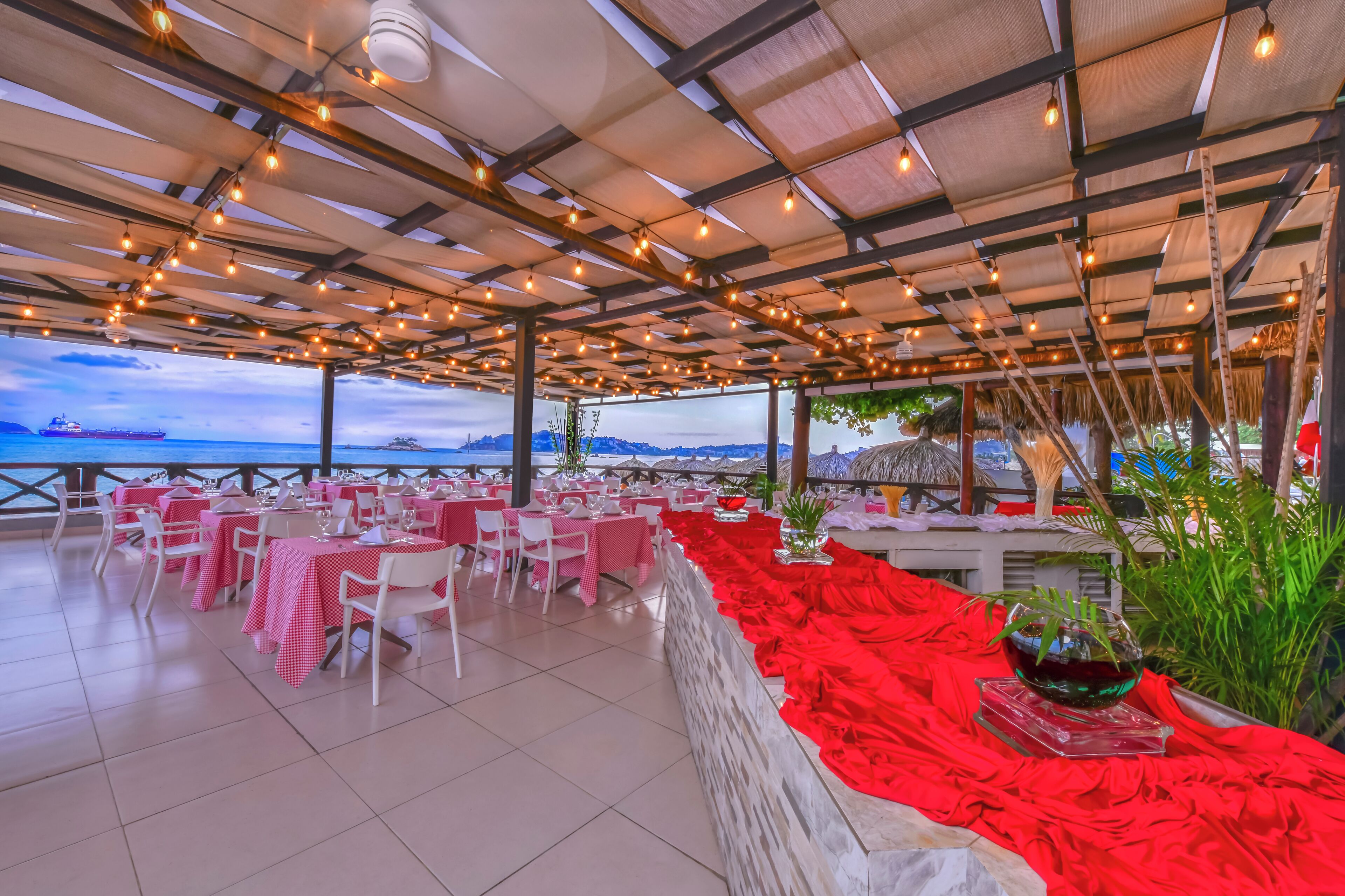 An outdoor dining area with tables and chairs, a red decorative border, and a view of the sea.