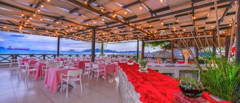 An outdoor dining area with tables and chairs, a red decorative border, and a view of the sea.