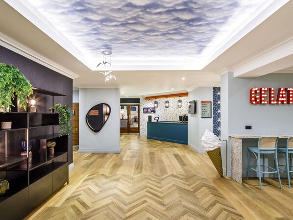 A hotel reception area with a modern design, including a herringbone wooden floor, a reception desk, and a wall-mounted sign. - ibis Styles Bournemouth (Bournemouth)