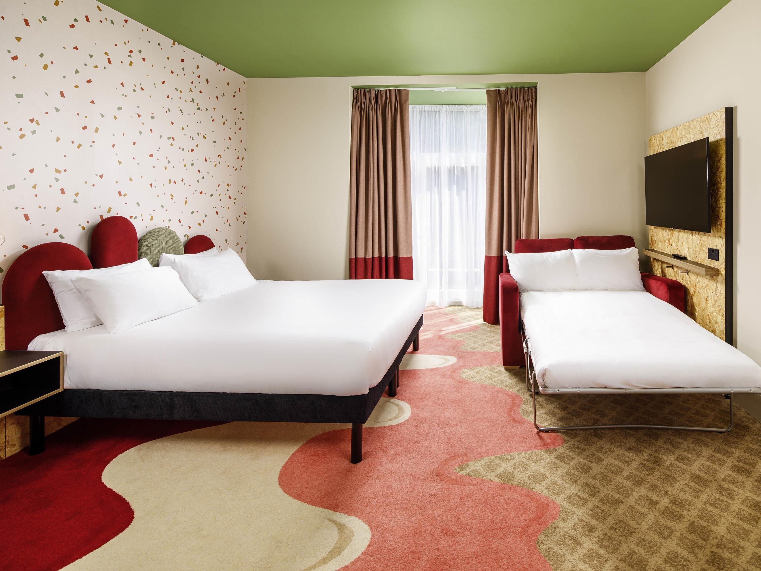Habitación de hotel con dos camas, televisión y ventana con cortinas.