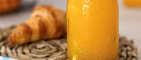 Een glas sinaasappelsap, een croissant en gestreepte rietjes op een geweven mat.