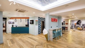 A spacious lobby with a wooden floor, a reception desk, a patterned wall, and a ceiling with a cloud design. - ibis Styles Bournemouth (Bournemouth)