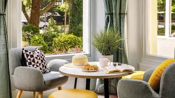 A cozy seating area with a round table, a potted plant, and a window with a view of greenery and a building.
