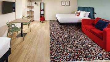 A hotel room with a bed, a red sofa, a dining table with chairs, a TV, and a patterned rug.