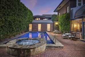 A swimming pool with a hot tub, surrounded by a brick patio and outdoor furniture.