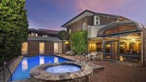 A swimming pool with a hot tub, a brick house, and a patio area with outdoor seating. - Adelaide Inn (North Adelaide)