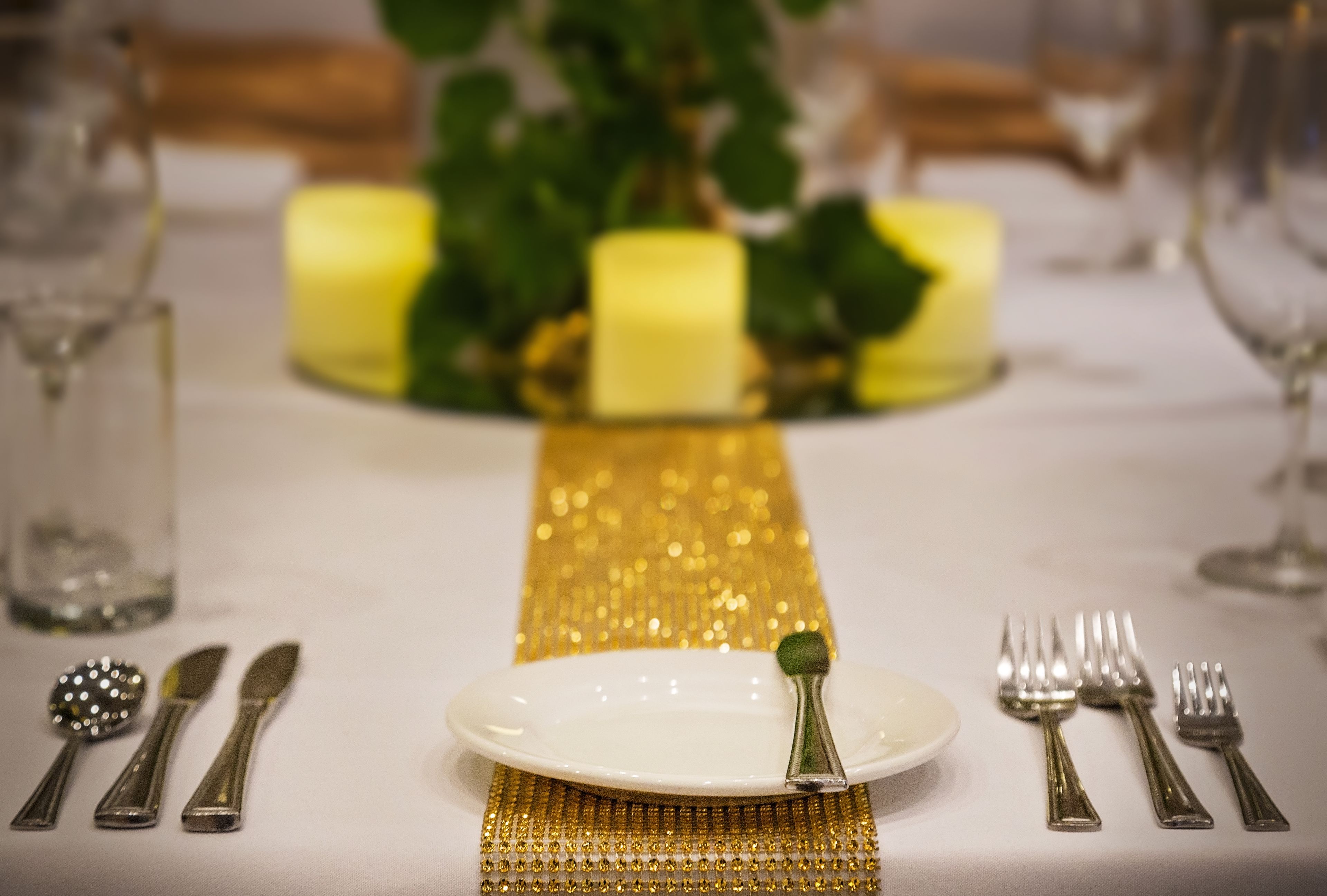 Una mesa dispuesta con un plato blanco, cubiertos y un mantel decorativo dorado.