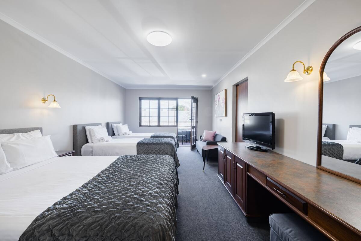A hotel room with two beds, a TV, a desk, and a large mirror.
