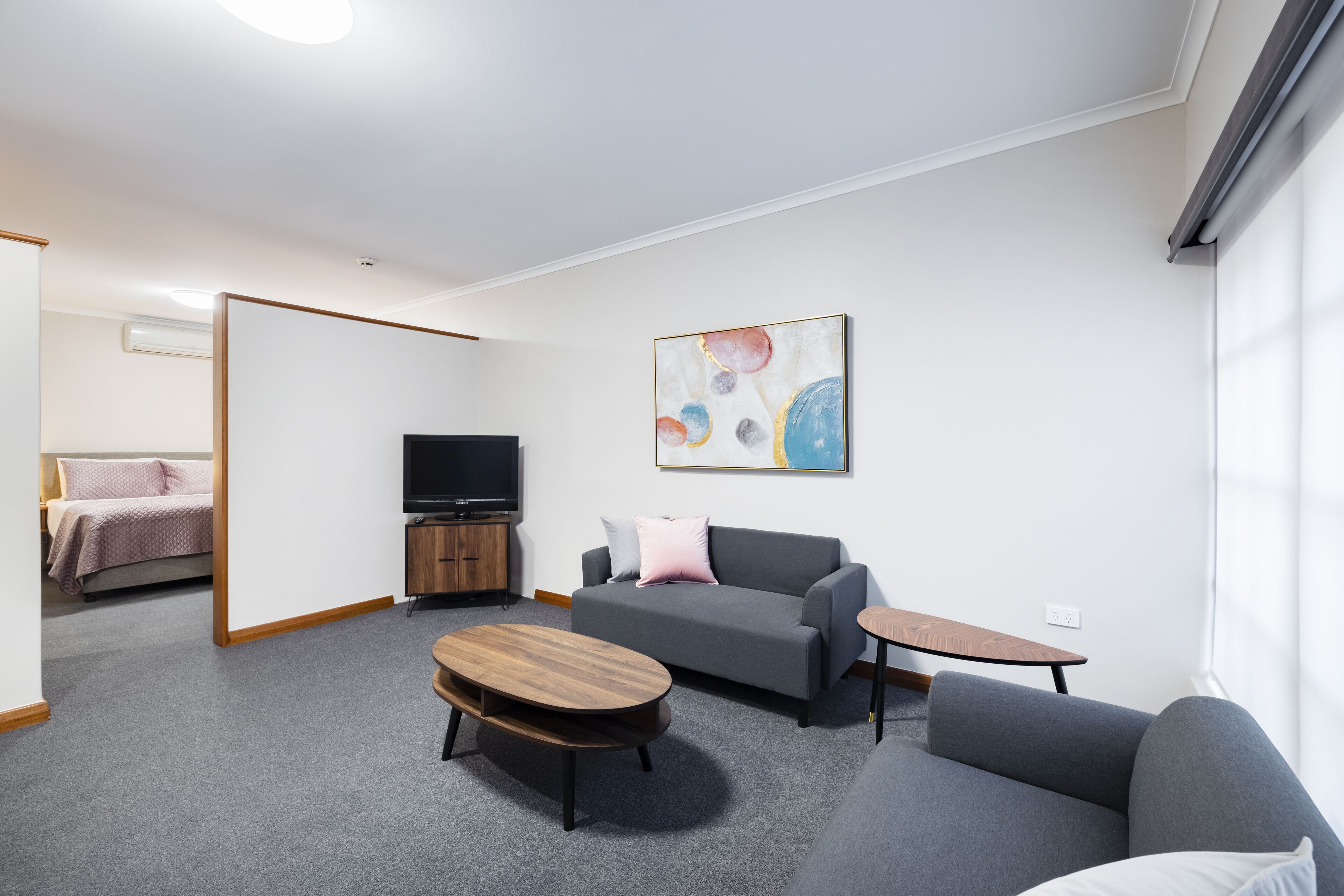 A modern living room with a grey sofa, a wooden coffee table, a TV, and a painting on the wall.