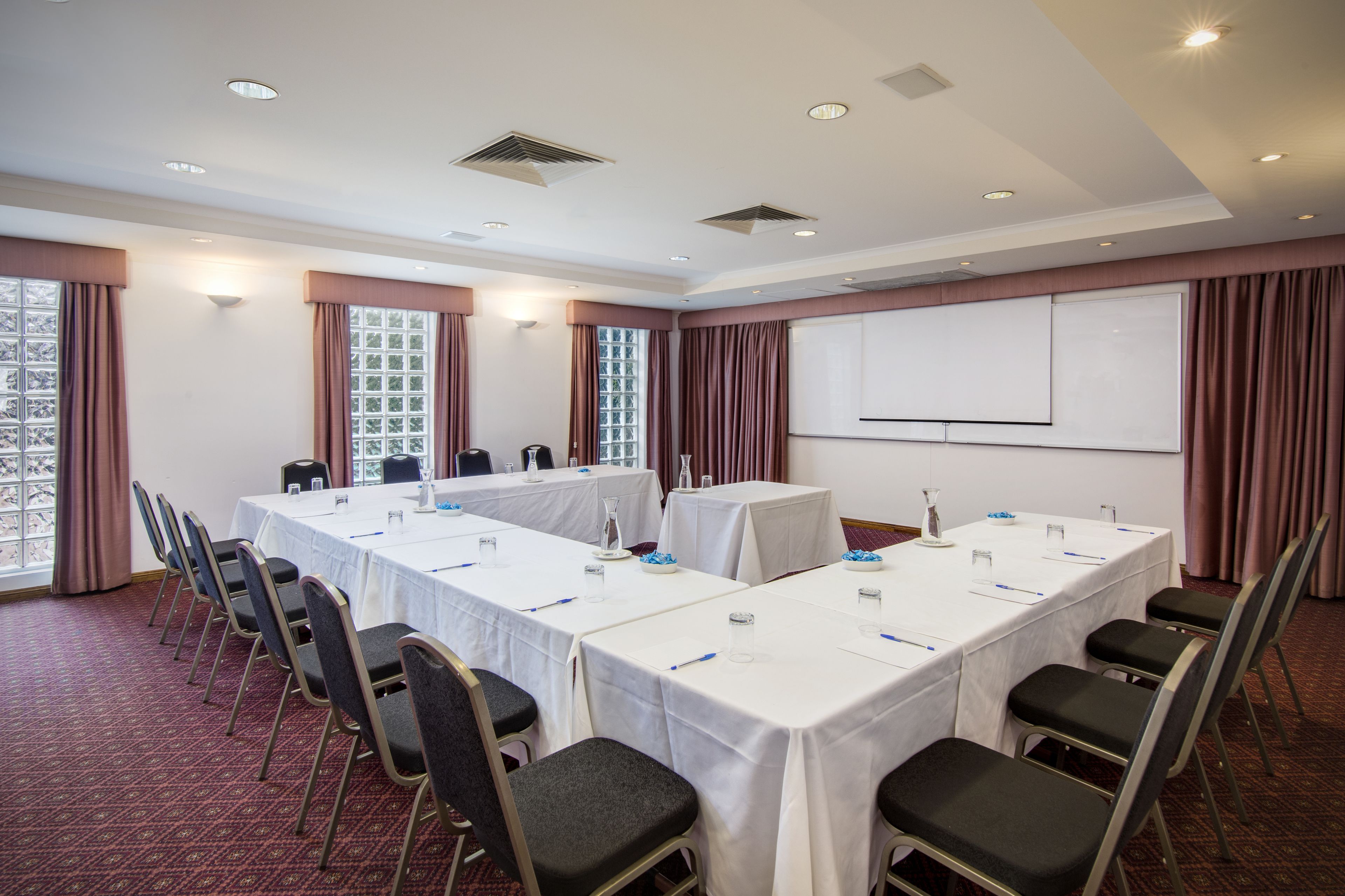 A conference room with long tables, chairs, and a projector screen.