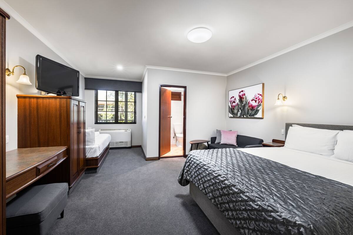 A hotel room with a bed, a desk, a television, a window, and a door leading to the bathroom.