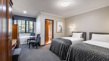 A hotel room with two beds, a desk, a chair, and a wardrobe.