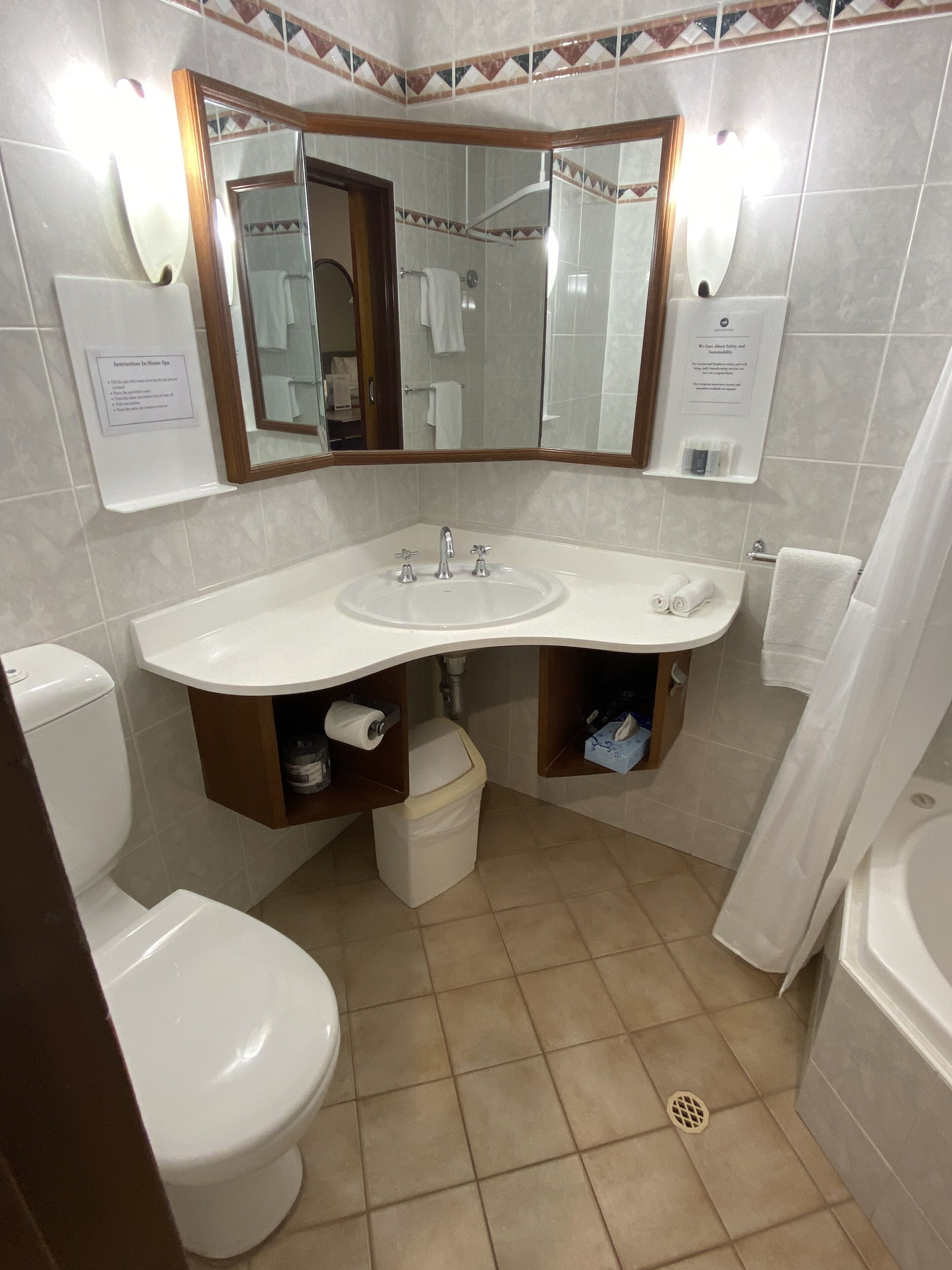 Un baño con lavamanos blanco, espejo y retrete. Hay dos toalleros y una cortina de ducha.