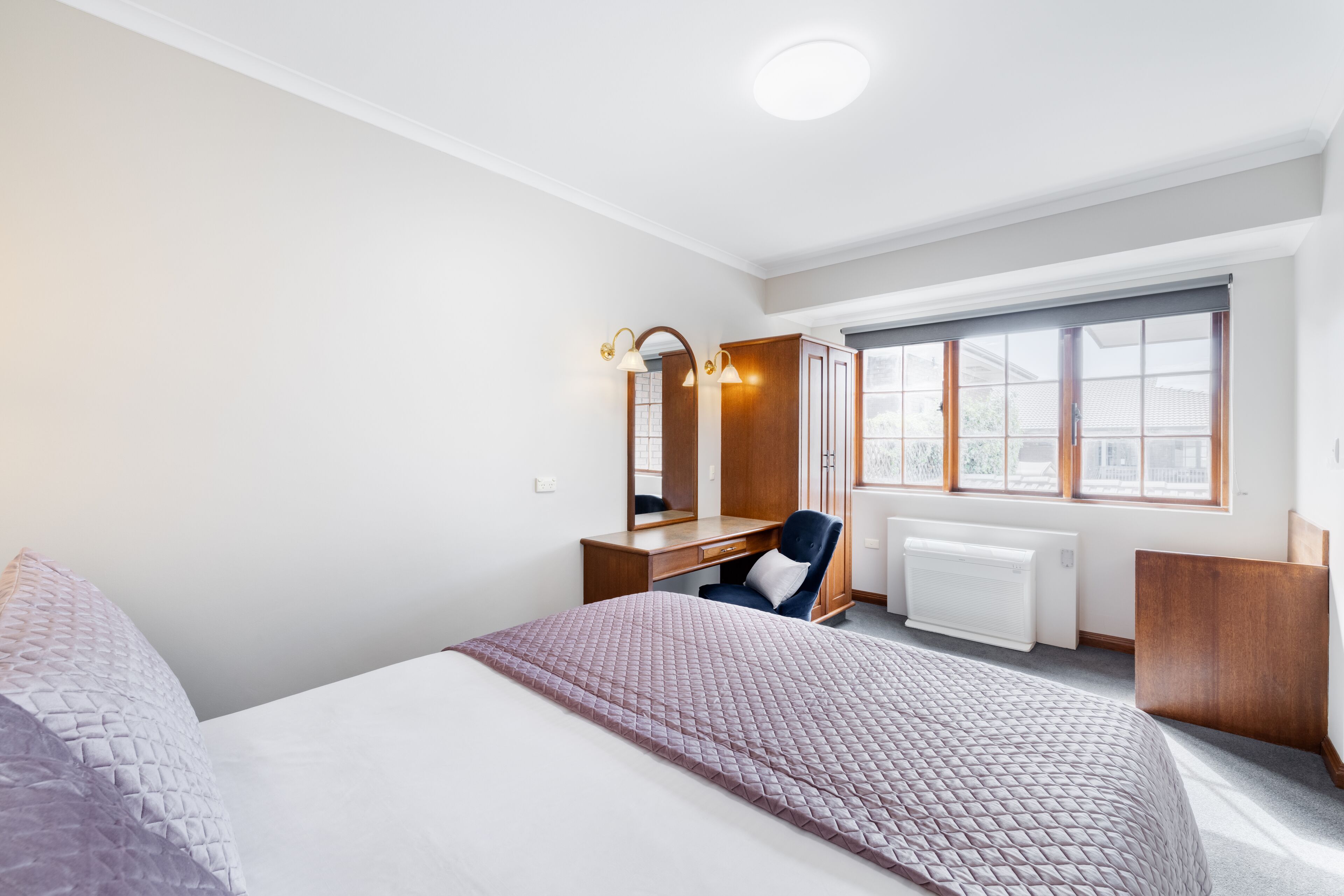 Een hotelkamer met een bed, een bureau, een stoel, een groot raam en een radiator.