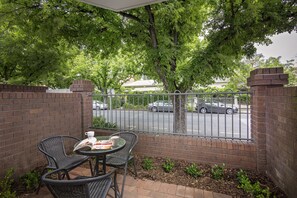 A patio with a brick wall, a table with chairs, and a view of a street with cars and trees.