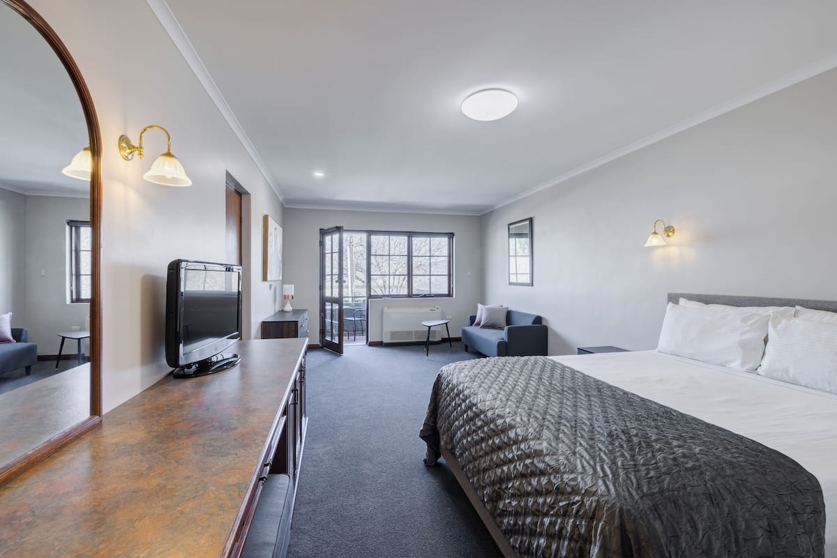 A hotel room with a large bed, a TV, a desk, and a mirror.