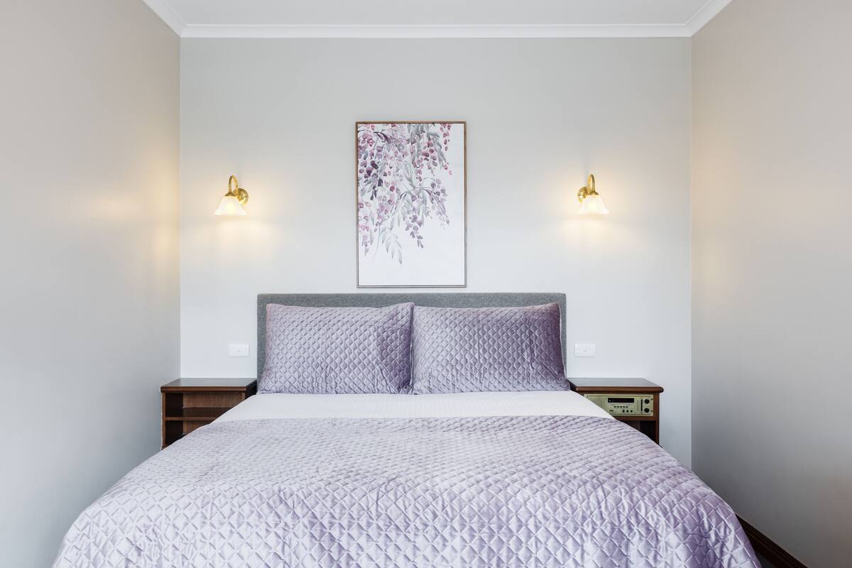 A neatly made bed with a quilted cover, two bedside tables with lamps, and a framed artwork on the wall.