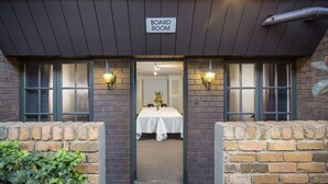 A board room with a table set for dining, two wall-mounted lamps, and a sign above the entrance. - Adelaide Inn (North Adelaide)