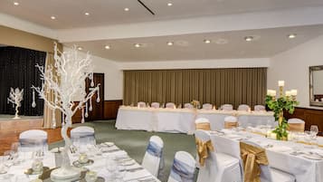 Un salón de banquetes con mesas redondas dispuestas para un evento formal, con manteles blancos, cintas doradas y un centro de mesa decorativo con un árbol blanco.