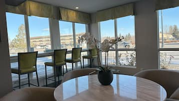 Ein Hotelzimmer mit großen Fenstern, einem runden Marmortisch und gelben Stühlen.