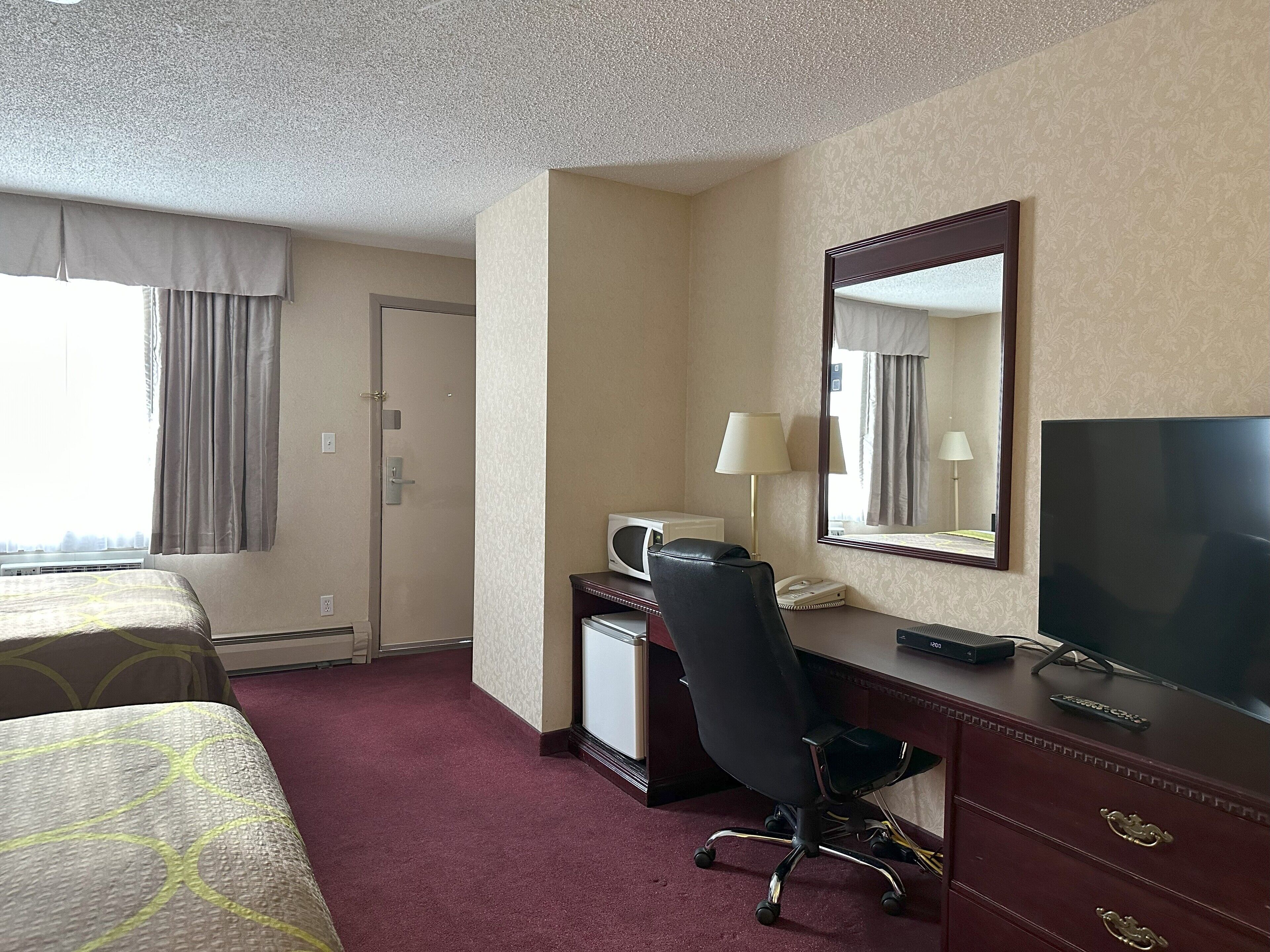 Habitación de hotel con dos camas, un escritorio con computadora, televisión, espejo y ventana con cortinas.