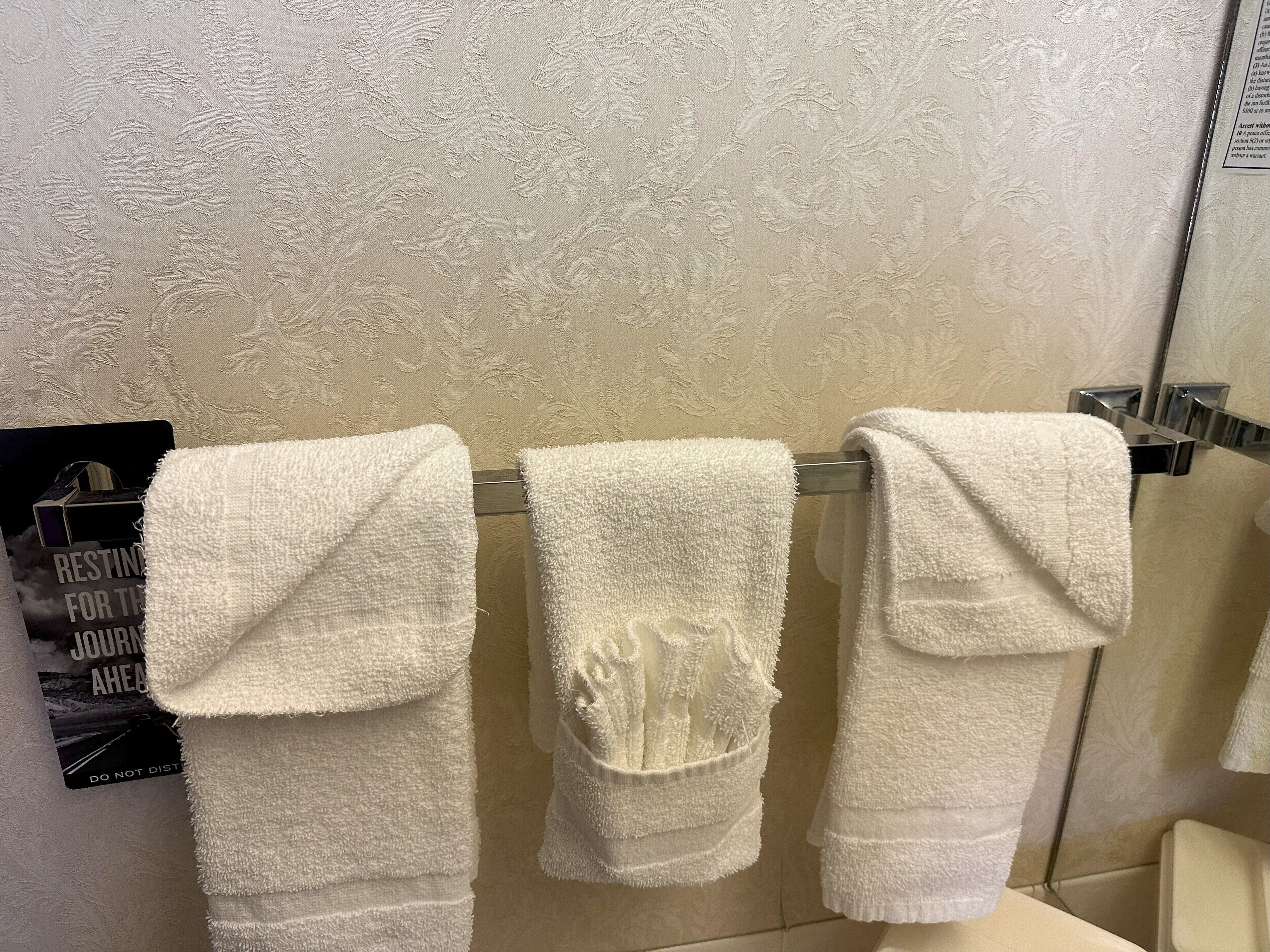 Un baño con tres toallas blancas colgadas en un perchero de metal frente a una pared con textura.