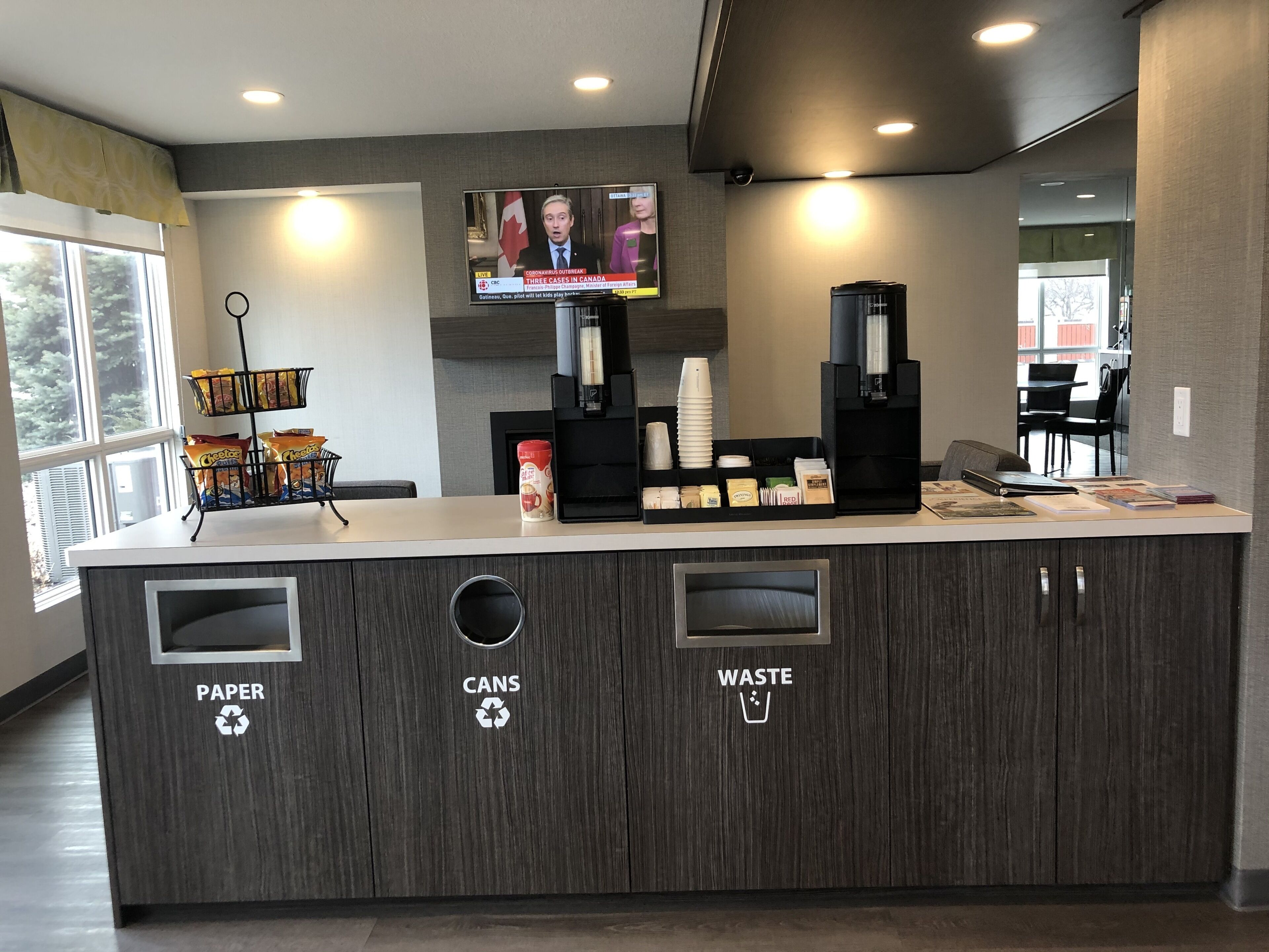 A reception desk with recycling bins labeled PAPER, CANS, and WASTE. A television displays a news broadcast.