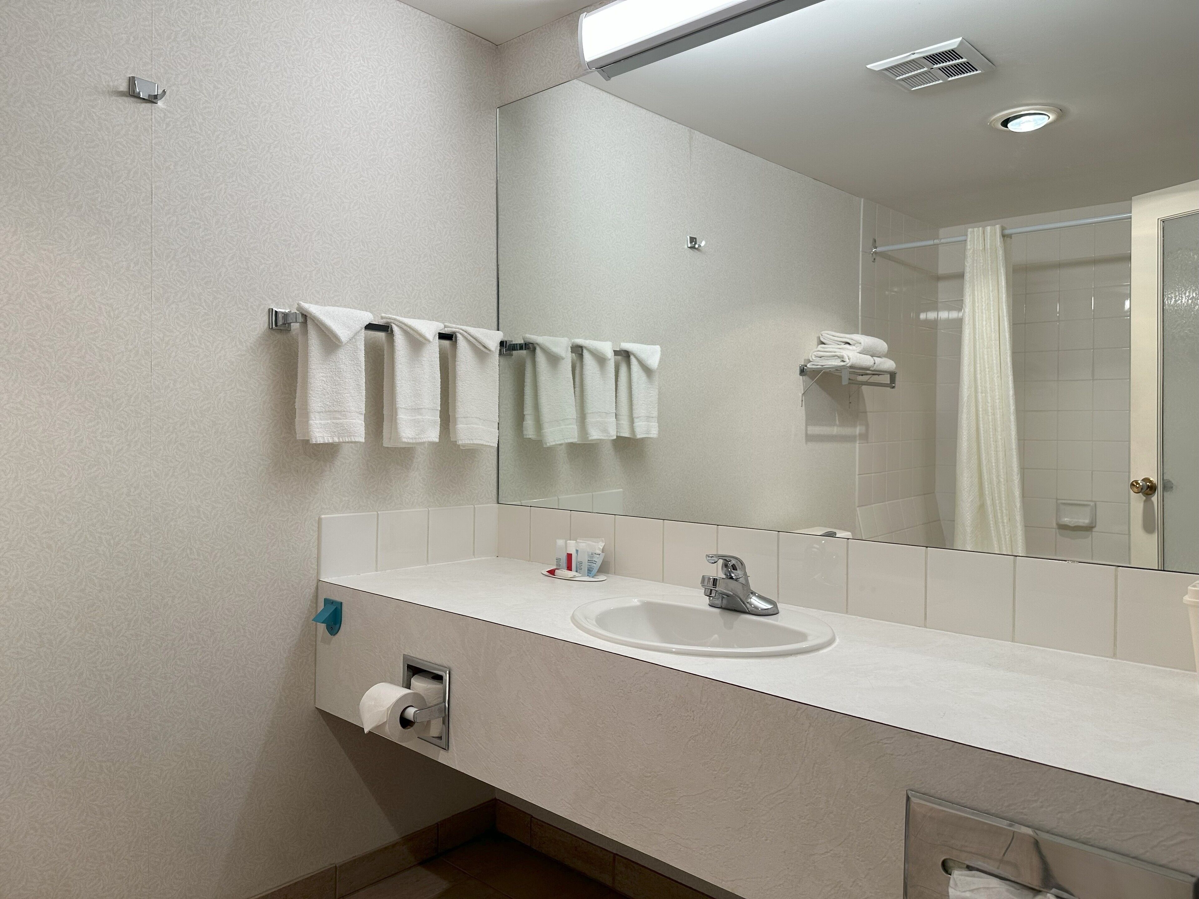 Un baño moderno con un espejo grande, lavamanos blanco y un perchero para toallas.