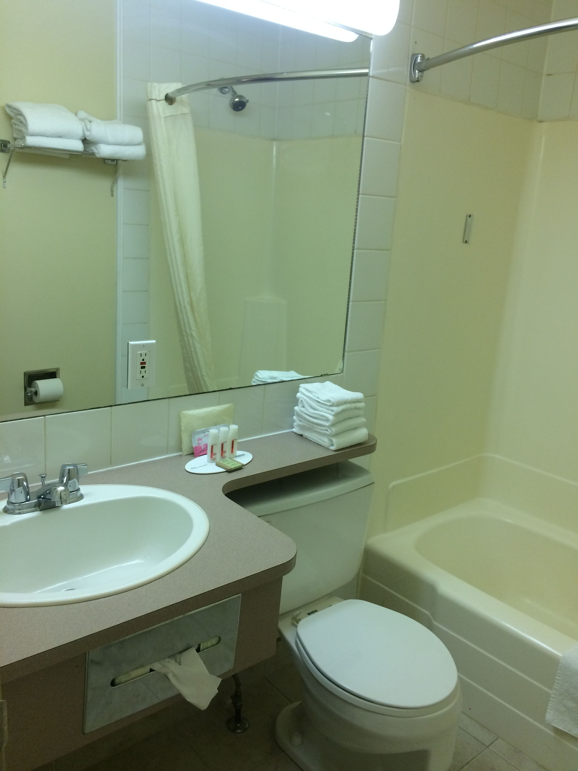 A bathroom with a sink, toilet, and bathtub. There are towels stacked on a shelf, and a shower curtain is visible.