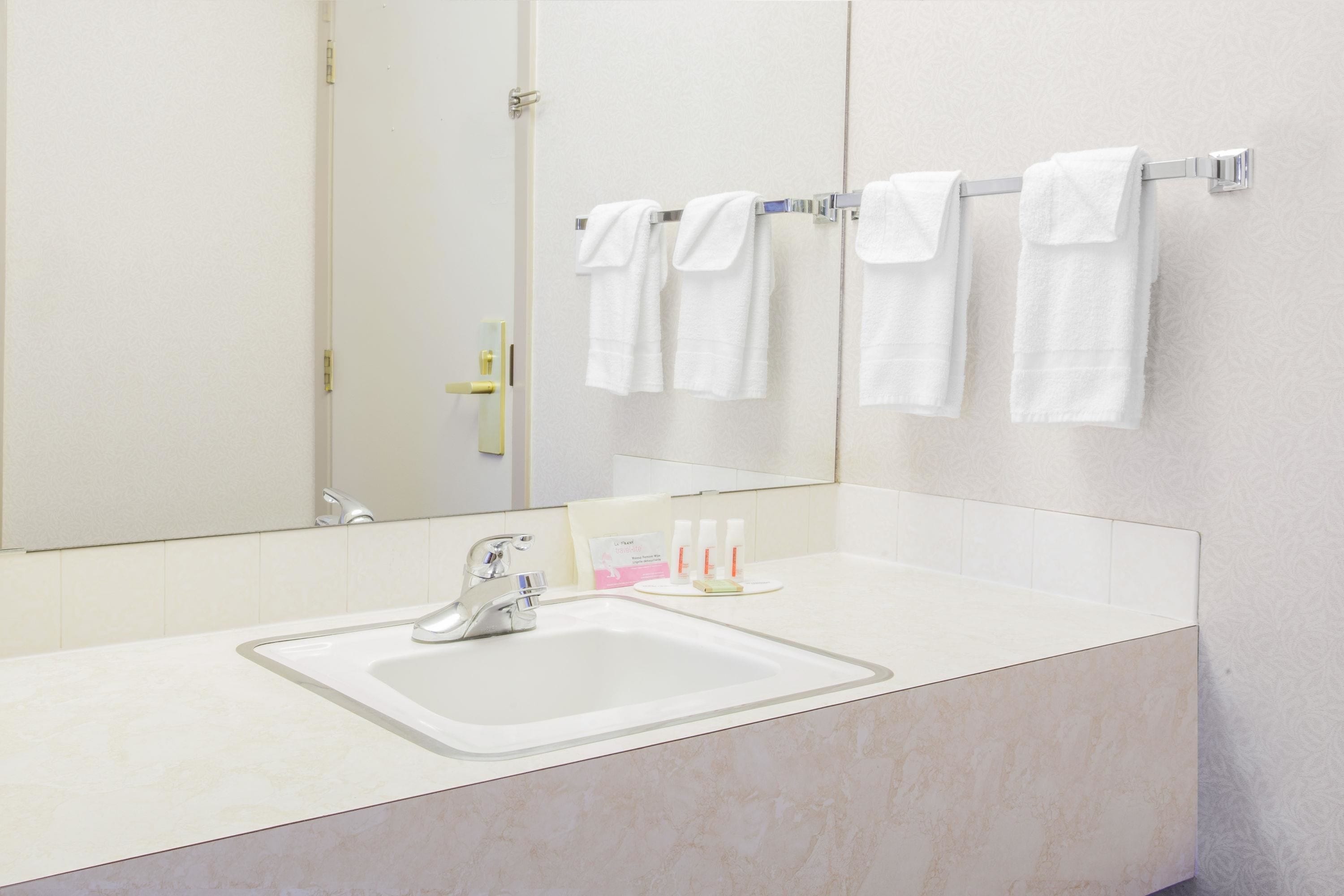 A bathroom with a white sink, a mirror, and three white towels hanging on a towel rack.