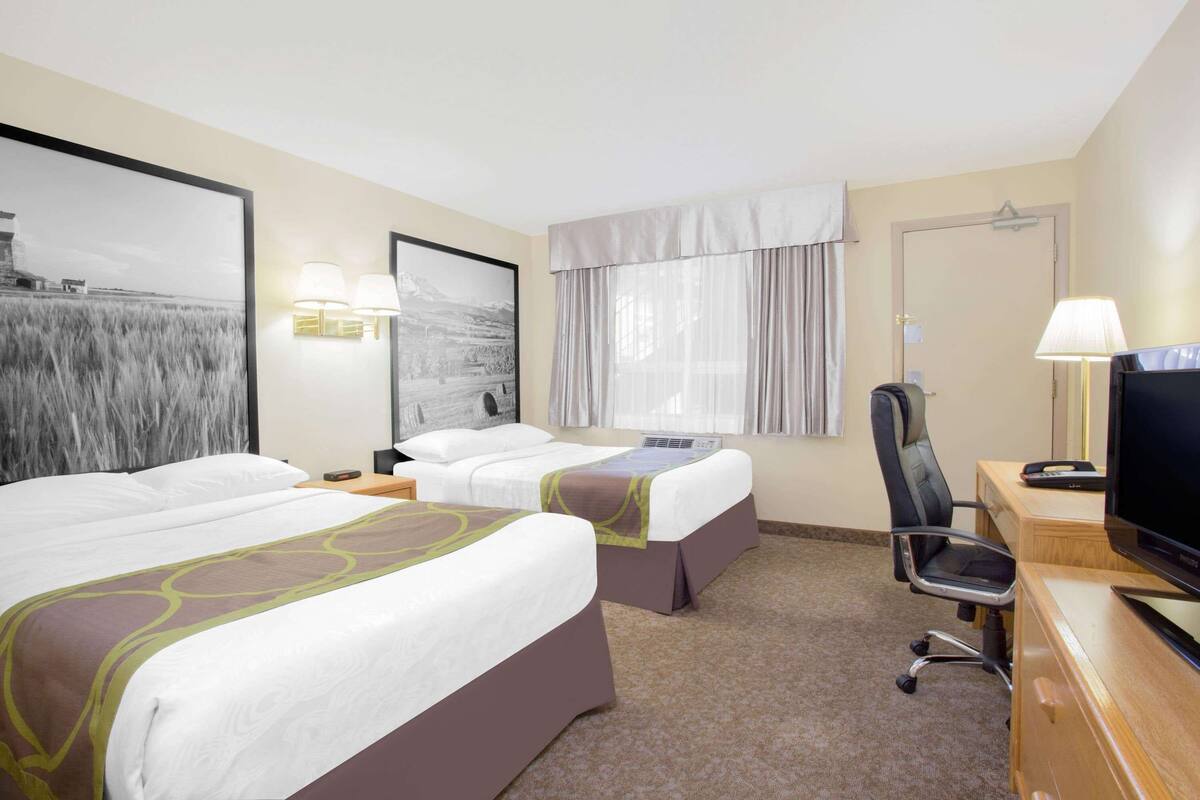 Habitación de hotel con dos camas, un escritorio con televisor, una silla y una ventana con cortinas.