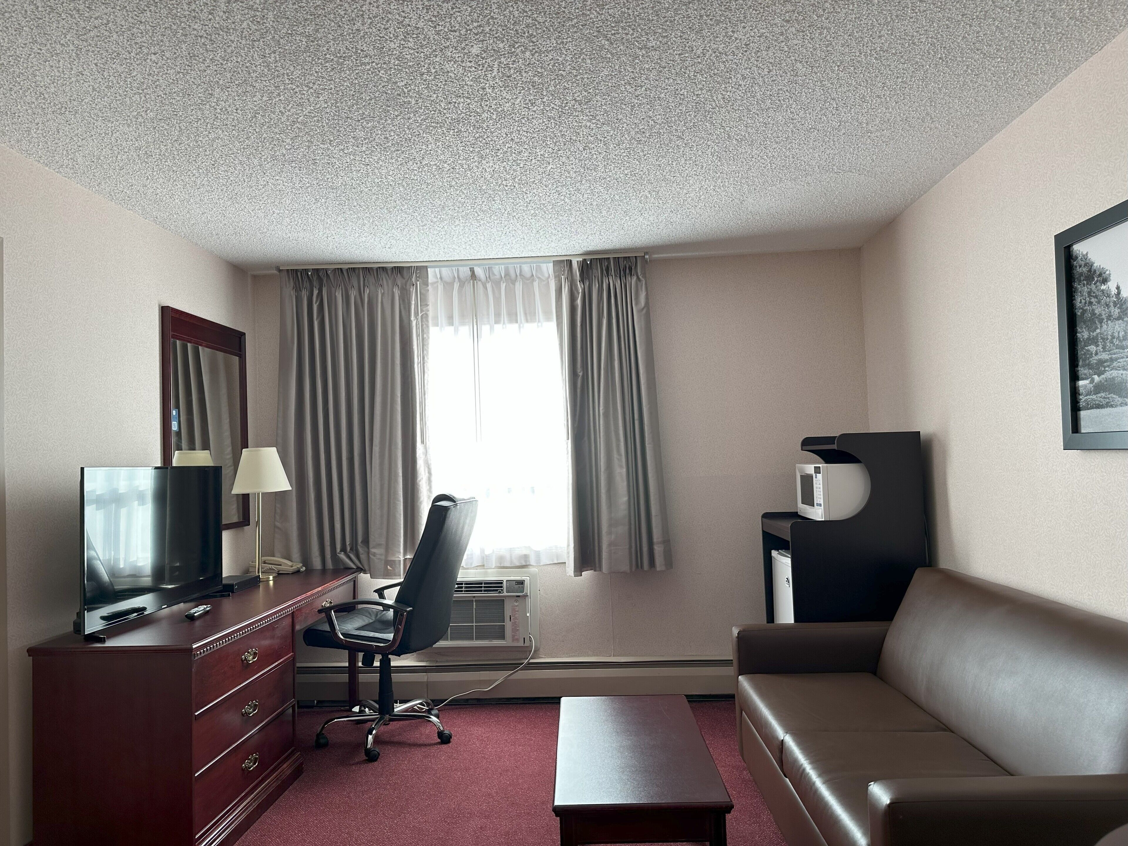 A hotel room with a television, desk, chair, sofa, and a picture on the wall.