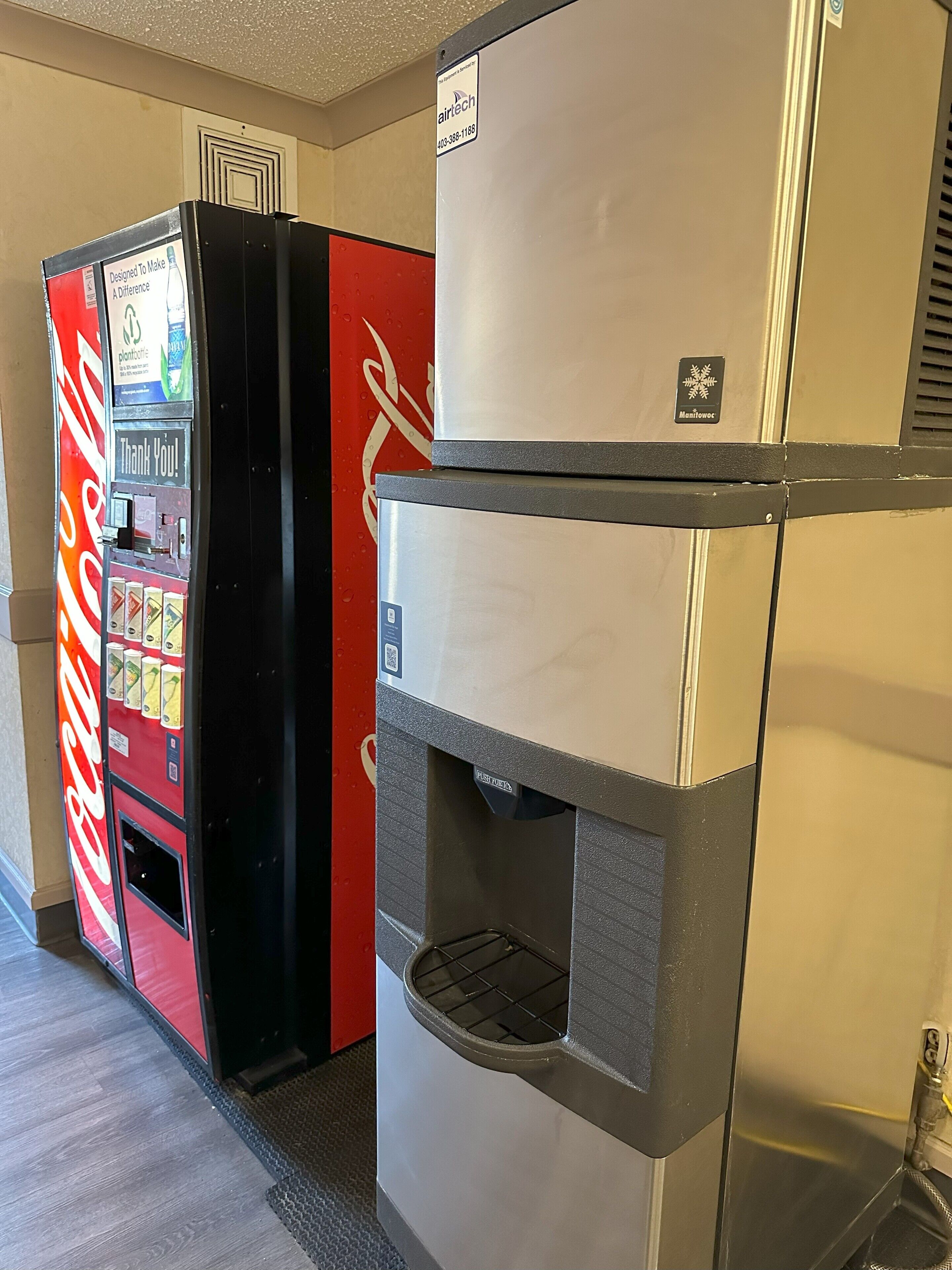 A vending machine with a Coca-Cola logo, a refrigerator with a water dispenser, and a sign indicating 'Manitowoc'.