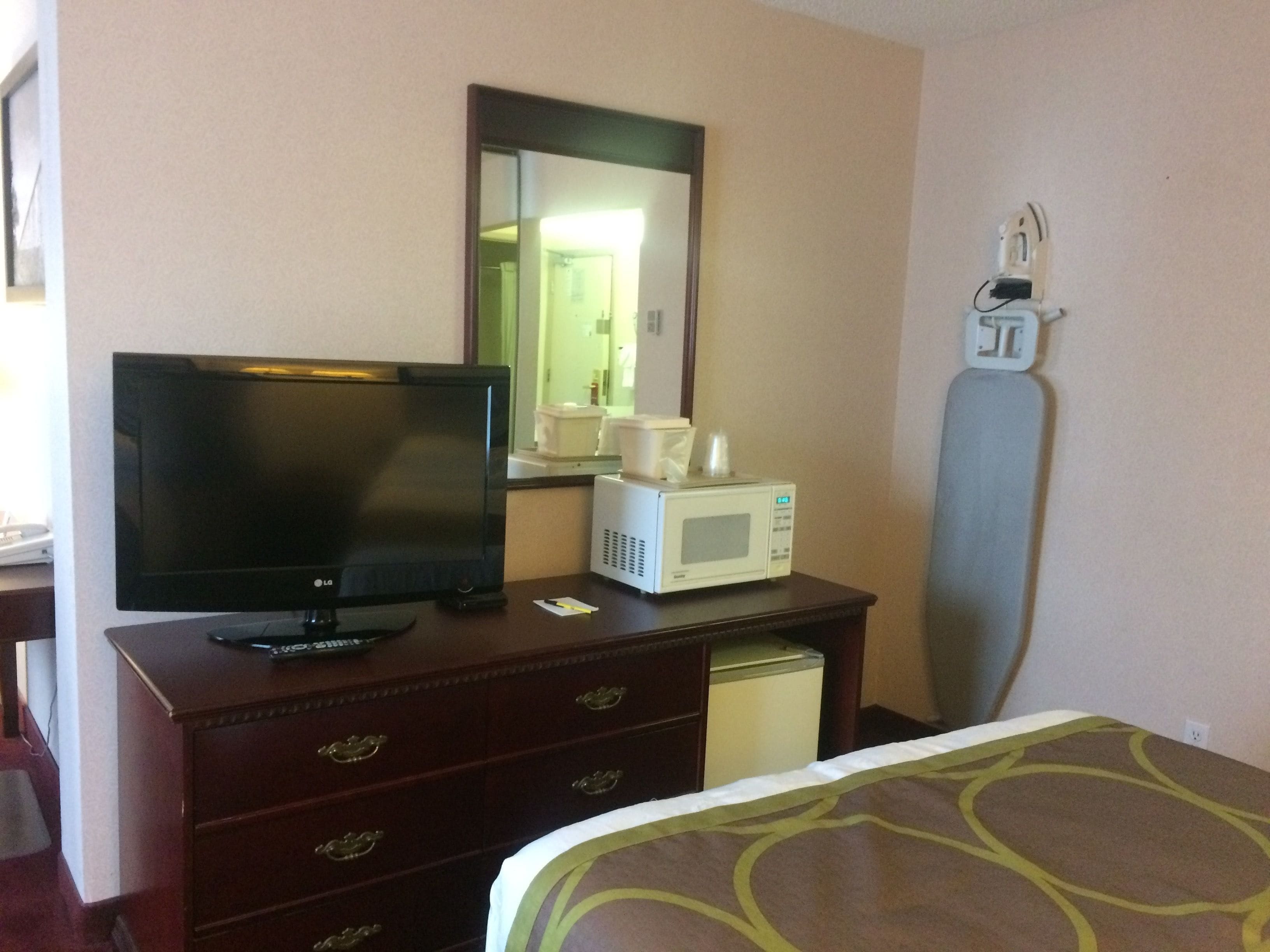 Una camera d'albergo con televisione sul comò, un forno a microonde e un letto con copripiumino decorato.