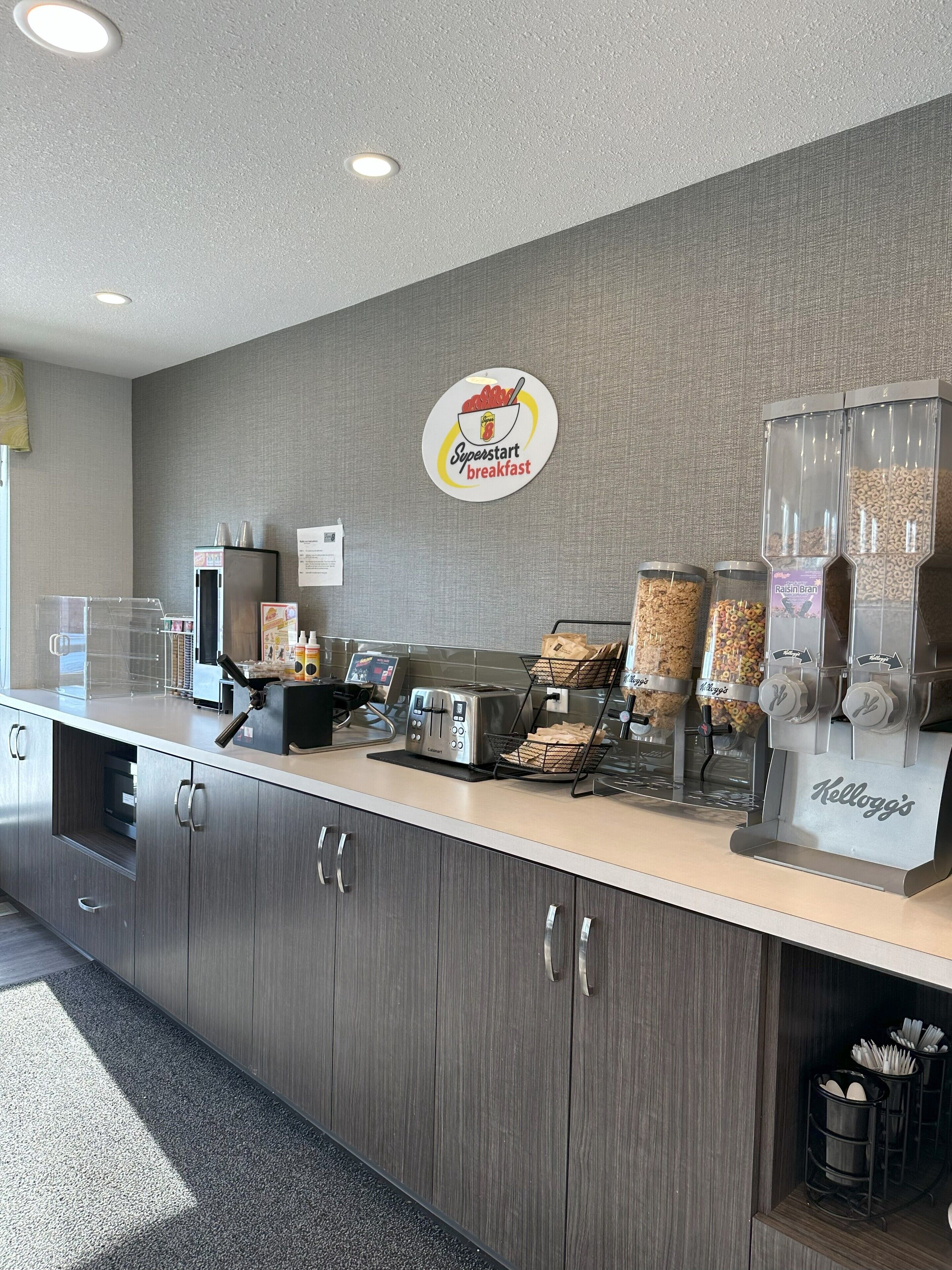 Una barra de desayuno con un tostador, dispensadores de cereales y un cartel que anuncia el desayuno Superstart.