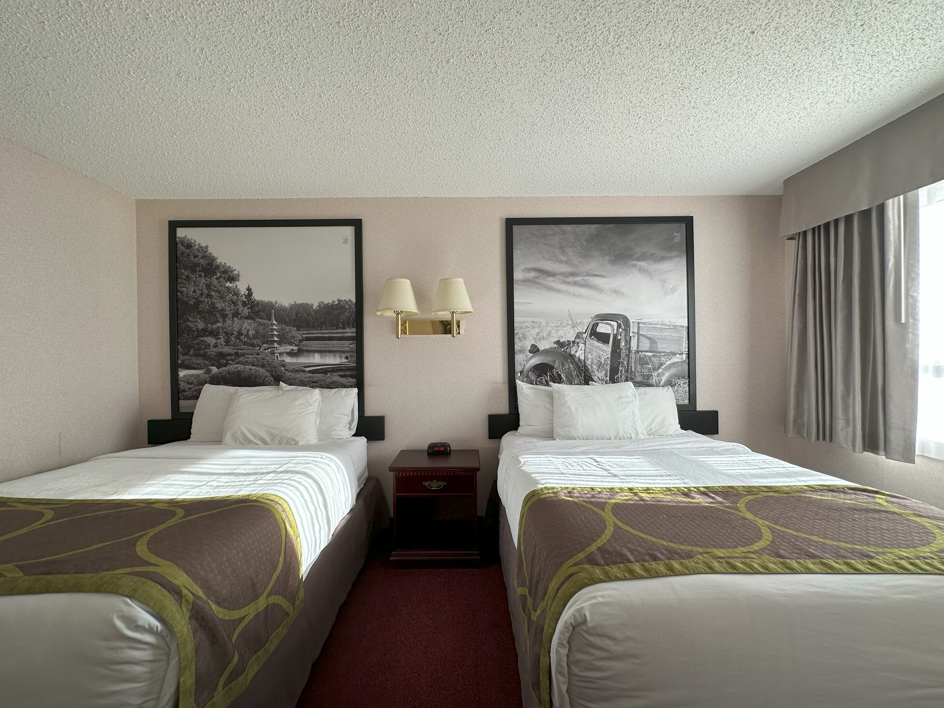 Une chambre d’hôtel avec deux lits, une table de chevet, une lampe et deux tableaux encadrés au mur.