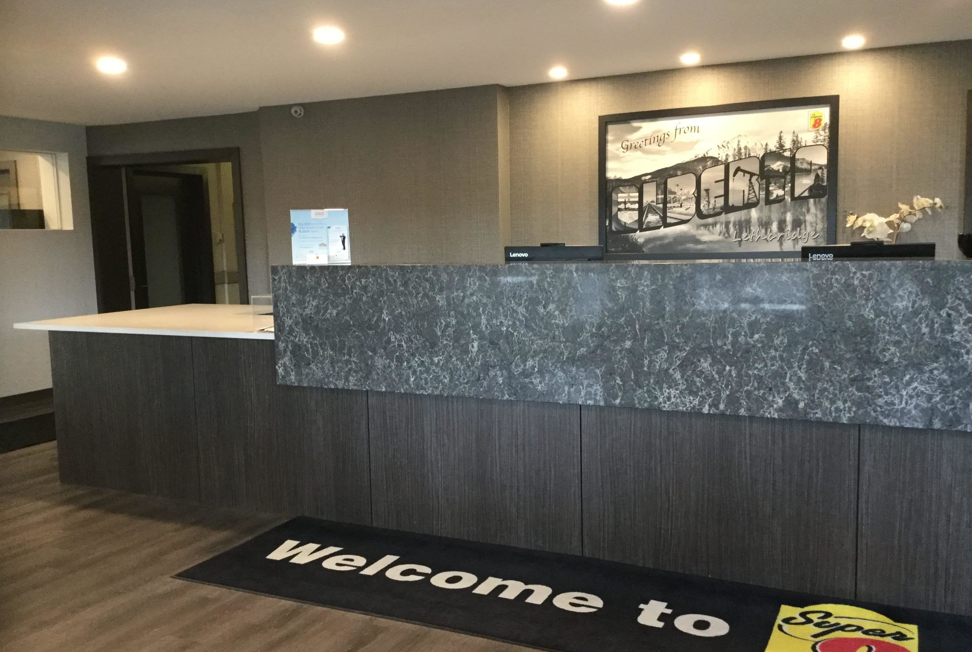 A reception desk with a marble top, a welcome mat, and a framed picture above the desk.