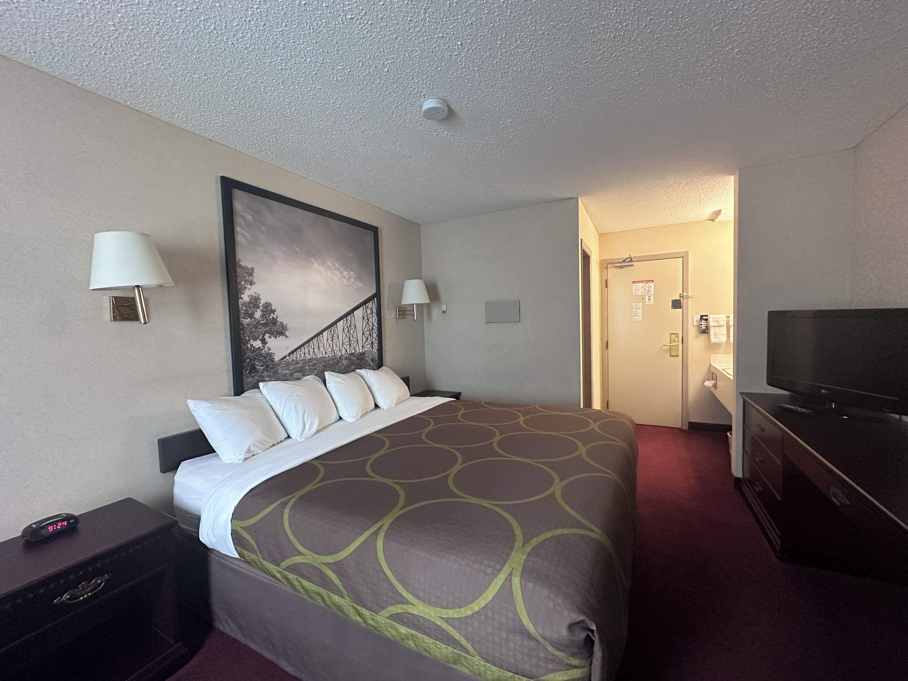 A hotel room with a large bed, two bedside lamps, a television, and a painting on the wall.