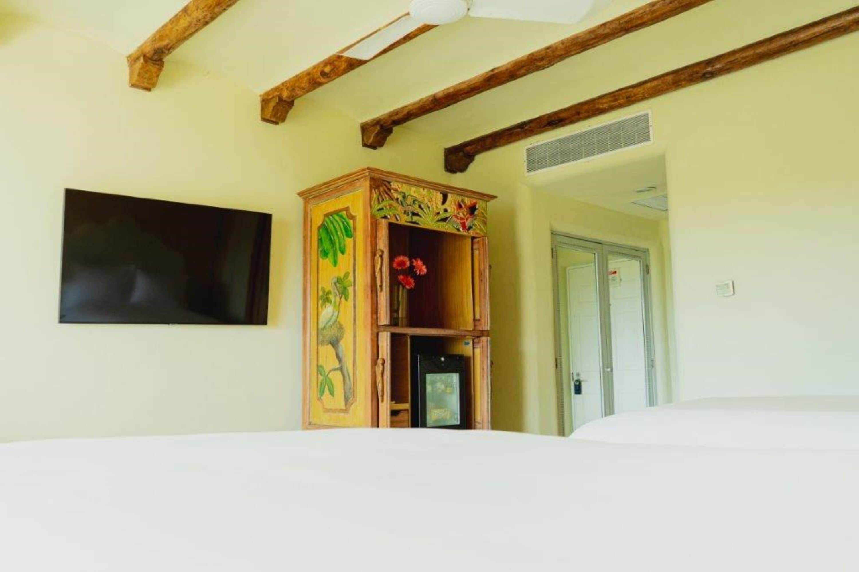A room with a bed, a wooden cabinet with floral carvings, a flat-screen TV, and a door.