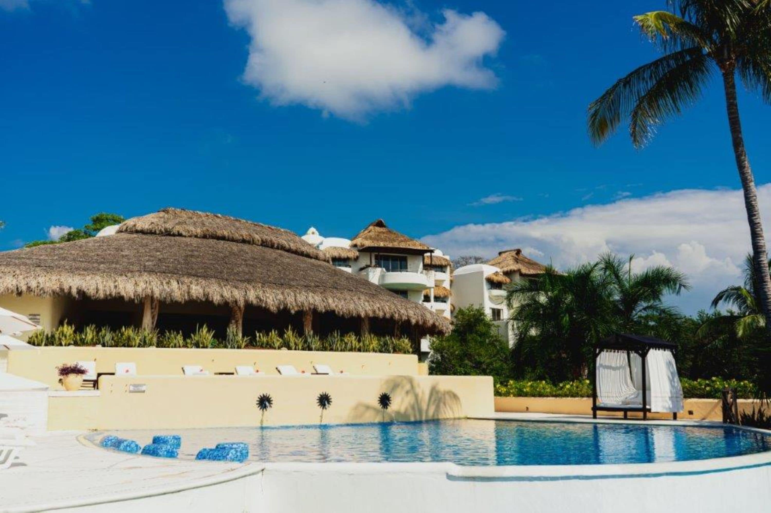 Un resort con piscina, construcciones de techo de paja y palmeras.