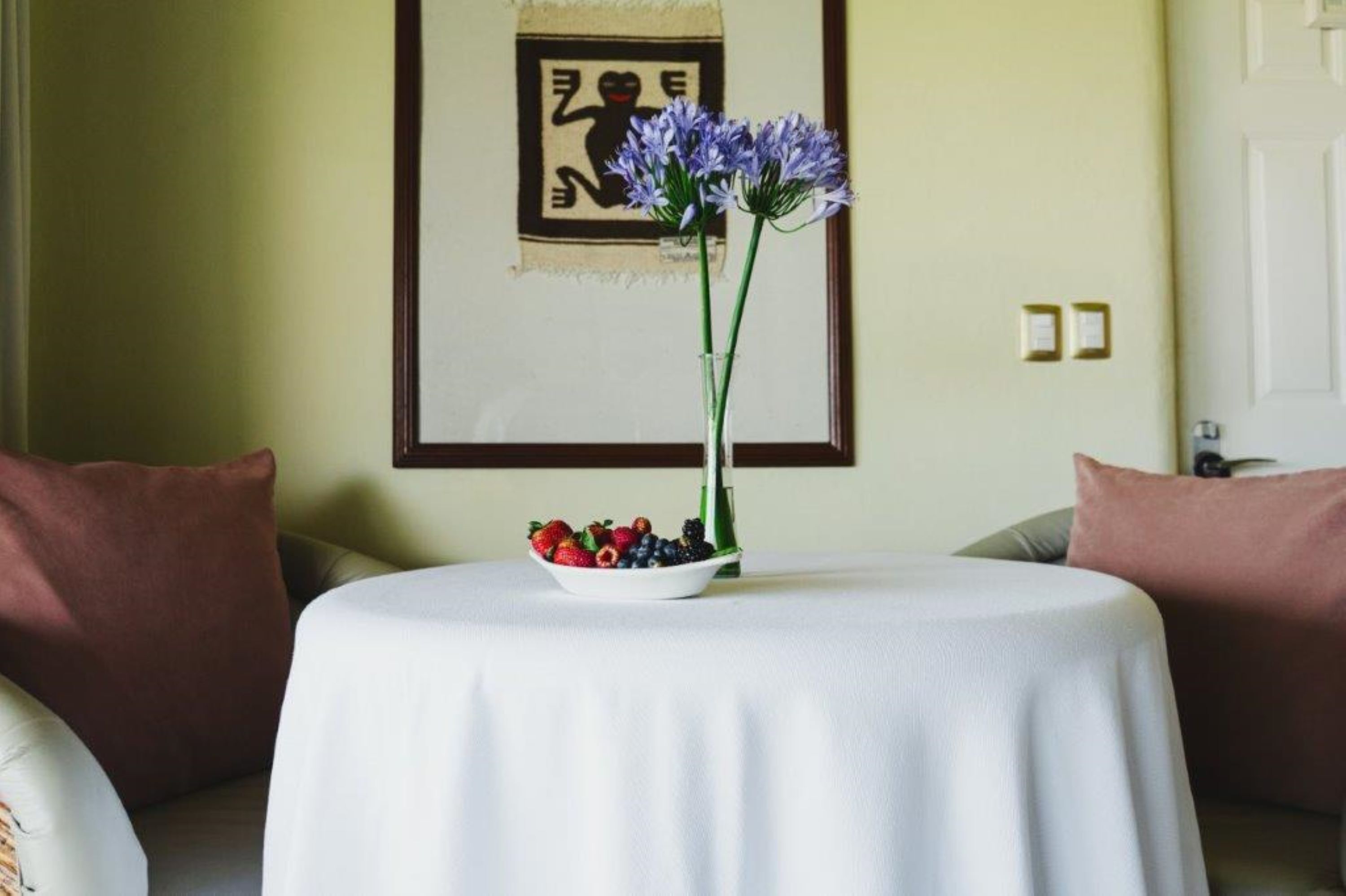 A round table with a white tablecloth, a bowl of fruit, and a vase with flowers.