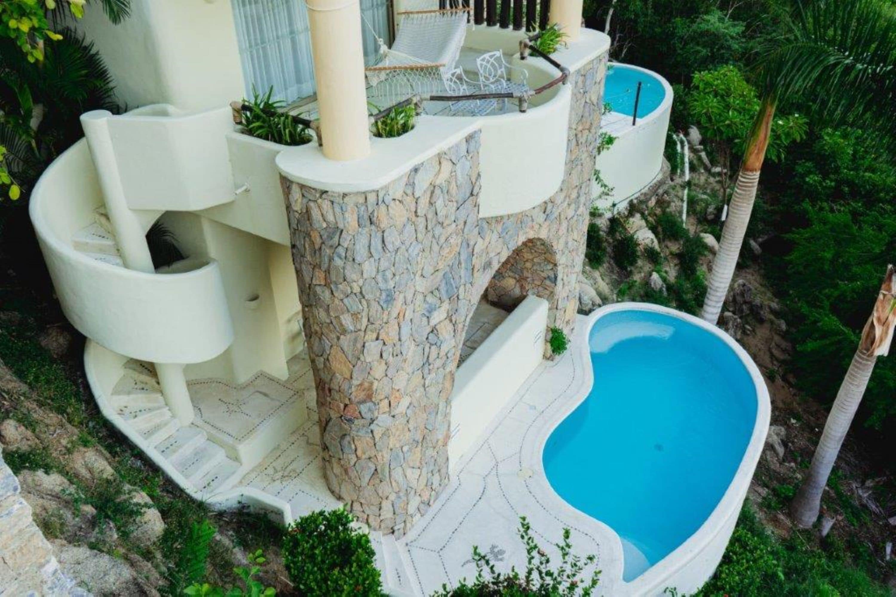 A poolside area with a stone pillar, a white lounge chair, and a blue pool.