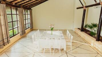 Una habitación amplia con techo alto, una gran mesa de comedor preparada para seis personas y vistas a zonas verdes a través de amplios ventanales.